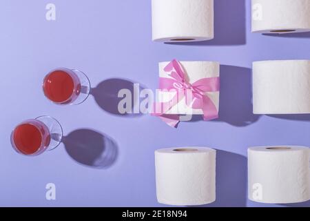 Paar Gläser mit Wein, Toilettenpapier als Geschenk in einem rosa Band. Auf einem lila Hintergrund. Draufsicht Stockfoto