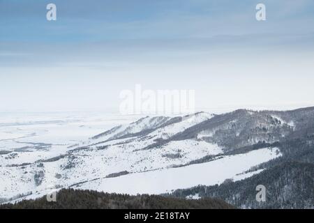 Sanfte Hänge der Waldhügel sind mit ersten Schnee bedeckt. Blick auf Bergtäler und Bergrücken am Horizont. Stockfoto