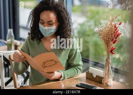 afroamerikanische Frau in der medizinischen Maske hält Menü im Café Stockfoto