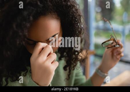 Müde afroamerikanische Frau mit geschlossenen Augen halten Brille Stockfoto