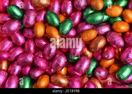 Große & kleine rosa, grün, orange und Bronze Folie verpackt Schokolade ostereier, vor einem pfirsichorange Hintergrund. Stockfoto