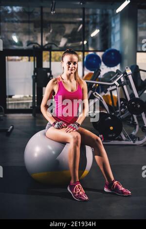 Fit schöne Form Mädchen sitzt auf einem Pilates-Ball entspannen nach dem Training im Fitnessstudio und Blick auf die Kamera. Stockfoto