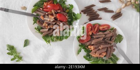 Buchweizen braune Pasta in weißen Schalen mit Tomaten, geräuchertem Lachs und Raketen Stockfoto