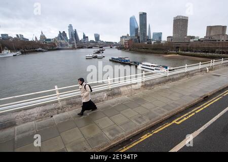 Eine Frau geht über eine nahe verlassene Waterloo Bridge im Zentrum Londons. Premierminister Boris Johnson ordnete eine neue nationale Sperre für England an, was bedeutet, dass die Menschen ihre Häuser nur aus begrenzten Gründen verlassen können, wobei die Maßnahmen bis Mitte Februar erwartet werden. Stockfoto