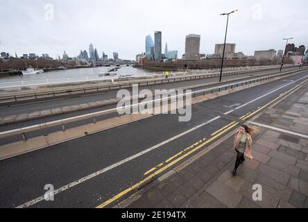 Eine Frau geht über eine nahe verlassene Waterloo Bridge im Zentrum Londons. Premierminister Boris Johnson ordnete eine neue nationale Sperre für England an, was bedeutet, dass die Menschen ihre Häuser nur aus begrenzten Gründen verlassen können, wobei die Maßnahmen bis Mitte Februar erwartet werden. Stockfoto