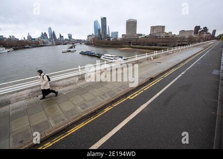 Eine Frau geht über eine nahe verlassene Waterloo Bridge im Zentrum Londons. Premierminister Boris Johnson ordnete eine neue nationale Sperre für England an, was bedeutet, dass die Menschen ihre Häuser nur aus begrenzten Gründen verlassen können, wobei die Maßnahmen bis Mitte Februar erwartet werden. Stockfoto