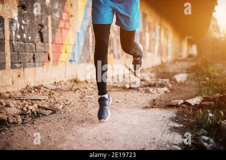 Junger, hübscher, sportlicher Mann, der bei Sonnenuntergang draußen läuft. Erfolgreicher junger aktiver Mann. Laufbeine. Stockfoto