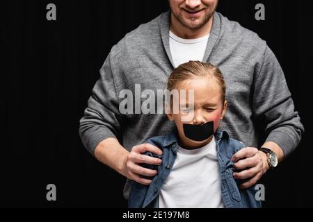 Lächelnd missbraucht umarmt Tochter mit Klebeband und Prellung isoliert Auf Schwarz Stockfoto