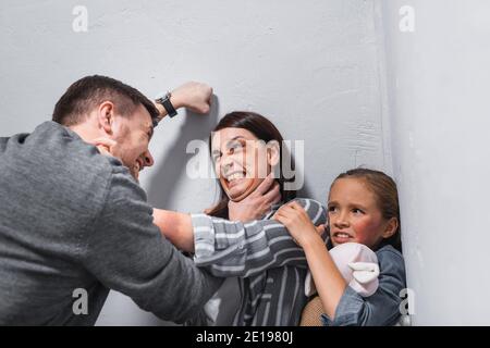 Wütend Mann würgen Frau mit Prellungen in der Nähe Tochter mit weich Spielzeug Stockfoto