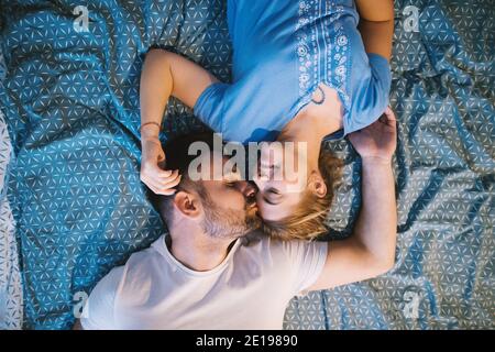 Fröhliche glücklich romantisches Paar auf dem Bett mit Körpern in entgegengesetzter Weise beim Kuscheln und Küssen liegen. Beziehungen und Wochenendziele. Stockfoto