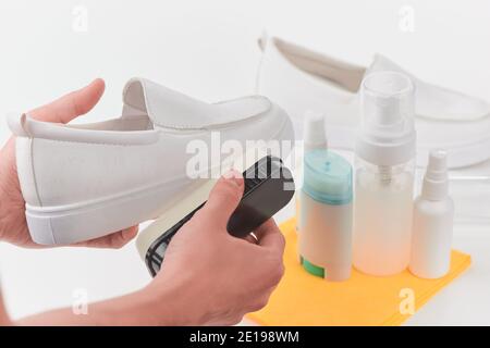 Hände entfernen Staub und Schmutz von einem weißen Lederloafer Mit einem Schwamm Stockfoto