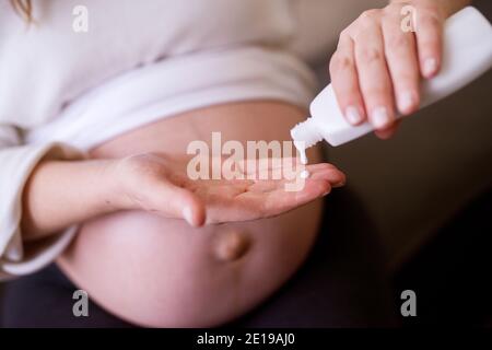 Schwangere Frau Gießen eine Creme auf die Hand, bevor sie auf ihren Bauch. Stockfoto