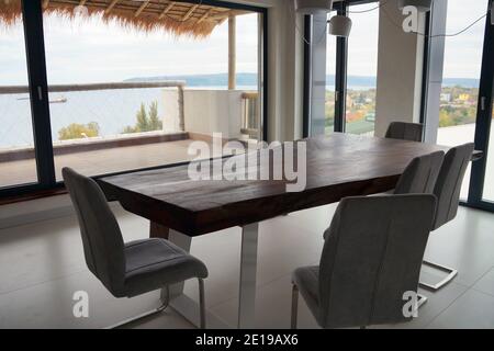 Esszimmer mit Holztisch und großen Fenstern mit Blick auf das Meer. Stockfoto