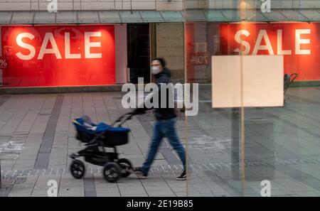 München, Deutschland. Januar 2021. Ein Mann mit einem Kinderwagen geht durch die fast leere Innenstadt an einem Laden vorbei, in dem das Wort "Sale" im Fenster hängt. Kredit: Peter Kneffel/dpa/Alamy Live Nachrichten Stockfoto