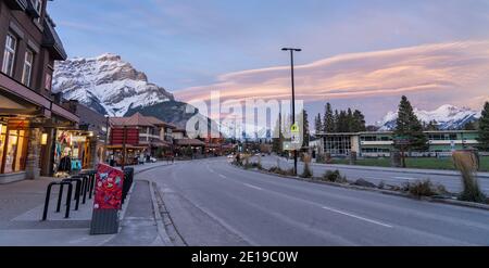 Blick auf die Straße von Banff Avenue am Herbstabend. Schneebedeckter Cascade Mountain mit rosa Himmel im Hintergrund. Stockfoto