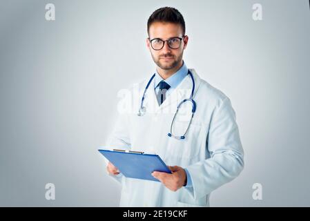 Studio-Portrait-Aufnahme von jungen männlichen Arzt hält Clipboard in der Hand, während er auf isolierten blauen Hintergrund. Stockfoto