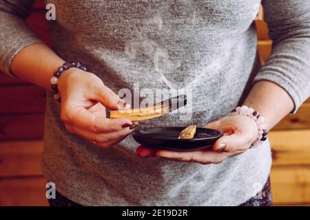 Frau Hände halten und mit Palo Santo Holzstäbchen Rauch für die Reinigung von zu Hause Sitzung von alten negativen Energie. Ölige aromatische heilige Holzstäbchen. Stockfoto