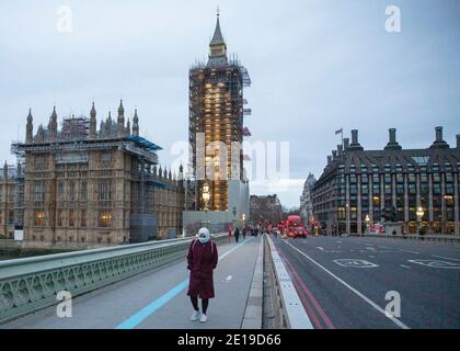 Eine maskierte Frau geht am Morgen des 5. Januar 2021 über eine ruhige Westminster Bridge im Zentrum von London, als die nationale Sperre wirksam wird Stockfoto