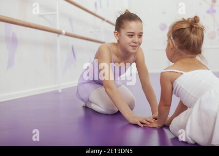 Schöne junge Ballerina hält Hände mit ihrer kleinen Schwester, Ruhe nach dem Training in der Ballettschule. Charmante junge Mädchen Ballett Tänzerin üben w Stockfoto