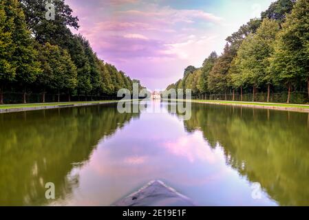 Schloss Lustheim (Teil der Schlossanlage Schleißheim) in der Abenddämmerung mit einem dramatischen violetten Himmel gesehen und im Gartenbrunnen reflektiert. Fotoaufnahme Stockfoto