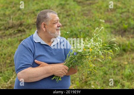 QSde sehen Portrait eines glücklichen älteren Mannes, der Strauß nimmt Von wilden Blumen und suchen Stockfoto