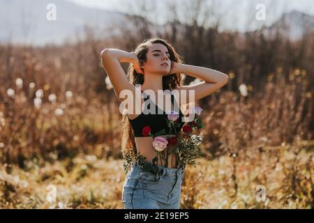 Junge schöne Frau mit langen Haaren in der Natur, verschiedene Arten von Blumen in Jeans, weibliche Gesundheit Konzept, genießen Sie die frische Luft Stockfoto