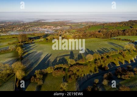 Luftdrohnenfoto der Cotswolds Hills mit Broadway im Tal, mit schönen ländlichen Aussichten, nebligen grünen Feldern und englischer Landschaft Landschaft im Nebel in Gloucestershire, England, Großbritannien Stockfoto