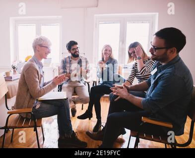 Junge Süchtige, die eine Situation feiern, während sie auf einer speziellen Gruppentherapie sitzen. Tapfere hartnäckige Kerl bekommen Applaus nach seinem Co Stockfoto