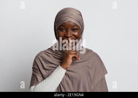 Geheimes Konzept. Junge arabische Frau in Hijab zeigt Stille Zeichen, setzen Finger auf Lippen, gestikulieren halten Stille über rosa Studio-Hintergrund, leeren Raum Stockfoto