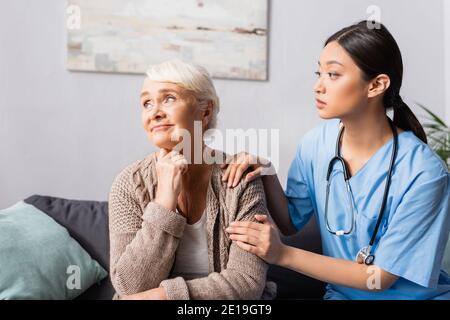 Junge asiatische Krankenschwester beruhigend verärgert ältere Frau sitzen und suchen Weg im Pflegeheim Stockfoto