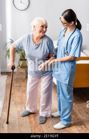 Ältere Frau mit Spazierstock Blick auf junge asiatische Krankenschwester Sie im Krankenhaus unterstützen Stockfoto