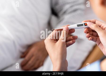 Teilansicht der Krankenschwester, die das Thermometer in der Nähe eines älteren Patienten hält, unscharfer Hintergrund Stockfoto