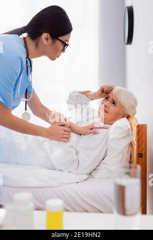 Junge asiatische Frau berühren kranke ältere Frau im Bett liegen und leiden unter Kopfschmerzen, verschwommen Vordergrund Stockfoto