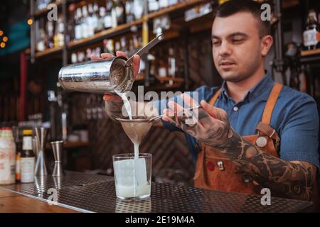 Tätowierte Barkeeper machen eine Dring für Kunden, Gießen Cocktail auf Eis in das Glas Stockfoto