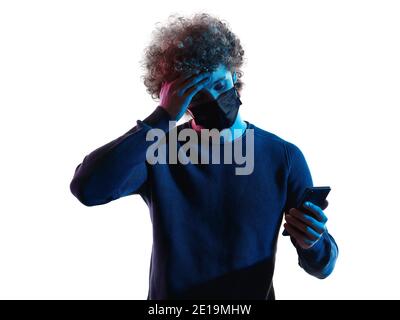 Ein kaukasischer junger Mann mit Kopfschuss Gesicht Porträt trägt eine Maske Verwendung von Telefon Sick im Studio Schatten isoliert weißen Hintergrund Stockfoto