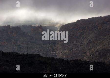 Morgensonne bricht durch bedrohliche Sturmwolken und erhellt die oberen Bergrücken der Cederberg Mountains, Südafrika, mit der Umgebung Stockfoto