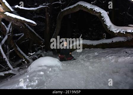 Yoga üben im Winter, im Wald bei Nacht im Schnee. Neue Herausforderungen mit Schnee und Kälte bringen dir bei, wie du Fokus und Kontrolle erreichst. Stockfoto