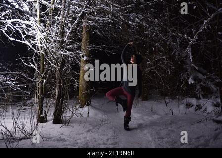 Yoga üben im Winter, im Wald bei Nacht im Schnee. Neue Herausforderungen mit Schnee und Kälte bringen dir bei, wie du Fokus und Kontrolle erreichst. Stockfoto