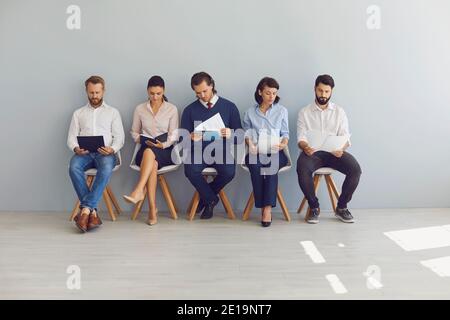 Gruppe von Arbeitssuchenden sitzen auf Stühlen in Reihe mit Lebensläufe und warten in der Schlange für das Interview Stockfoto