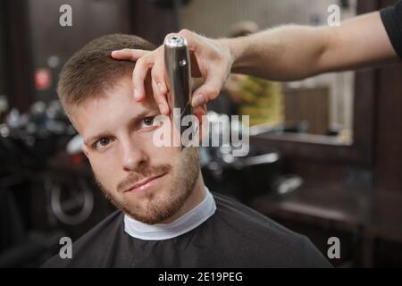 Fröhlicher Mann lächelt zur Kamera, während Friseur Trimmen seine Bart Stockfoto