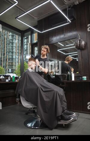 Vertikale voller Länge Schuss eines professionellen Friseur Föhnen Haare eines männlichen Klienten Stockfoto