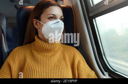Fahren Sie sicher mit öffentlichen Verkehrsmitteln. Junge Geschäftsfrau mit KN95 FFP2 Gesichtsmaske Blick durch Zugfenster. Zugpassagier mit Schutzmaske tr Stockfoto