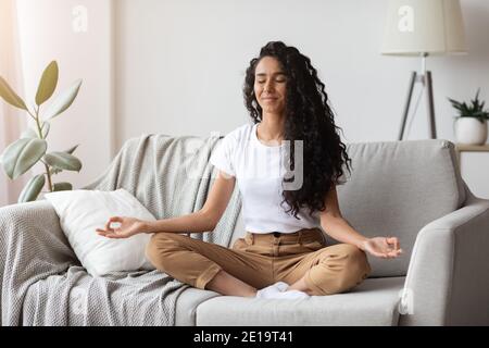 Friedliche Brünette Dame auf der Couch sitzend, meditierend Stockfoto