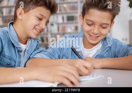 Eine kurze Aufnahme von zwei fröhlichen jungen Jungen, die gemeinsam in der Bibliothek studieren. Glückliche Zwillingsbrüder machen Hausaufgaben Stockfoto