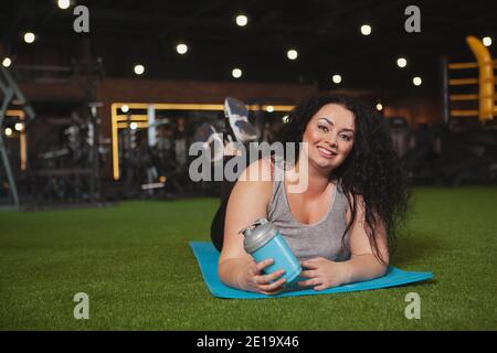 Fröhliche Plus Größe Frau entspannen im Fitnessstudio nach dem Training, liegend auf Yoga-Matte, kopieren Raum. Glücklich schöne übergewichtige Sportlerin, die beim Sport ruht Stockfoto