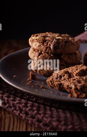 Dreifache Schokolade Chip Cookies mit Stücken von weißer Milch und Dunkle Schokolade mit dunkler kreativer Beleuchtung Stockfoto