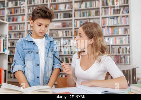 Verärgerte Mutter schimpft ihren Sohn in der Bibliothek. Verärgerte Mutter beschuldigt ihr Kind für schlechtes Benehmen oder Mark in der Schule Stockfoto