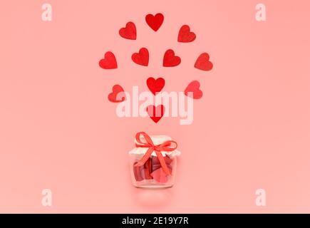 Rote Holzherzen im Glas mit Schleife Knoten auf rosa Pastell Hintergrund. Romantische Herzkomposition für Valentinstag oder Muttertag Karte Stockfoto