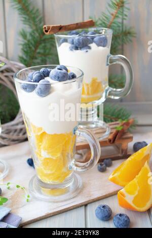 Hausgemachter griechischer Joghurt mit Heidelbeeren und Orange in einem Glas auf weißem Hintergrund, Health Food aus Joghurt Konzept. Vertikales Bild Stockfoto