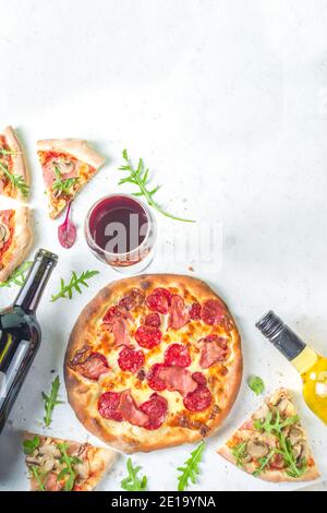 Pizza-Party-Konzept. Set von Pizzen mit verschiedenen Füllungen, Stücke von verschiedenen Pizza, Glas und Flasche mit Wein. Flatlay Draufsicht Kopieplatz auf weiß Stockfoto